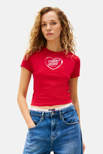 T-shirt rouge à manches courtes de TOMMY JEANS, avec un logo en forme de cœur blanc sur la poitrine, associé à un jean bleu.