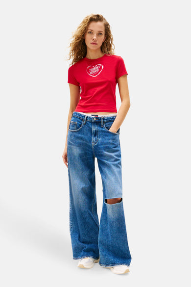 T-shirt rouge à manches courtes de TOMMY JEANS, avec imprimé en forme de cœur, associé à des jeans larges avec un trou au genou.