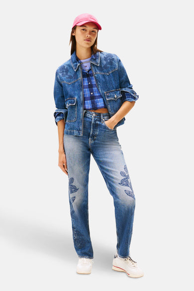 Jean de blauw denim de TOMMY JEANS, avec des motifs floraux et associé à une blouse fluide et un chapeau rose.