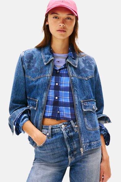 Veste en jean denim bleu moyen de Tommy Jeans, avec broderie florale sur les épaules, combinée avec une chemise à carreaux bleus et une casquette rose.