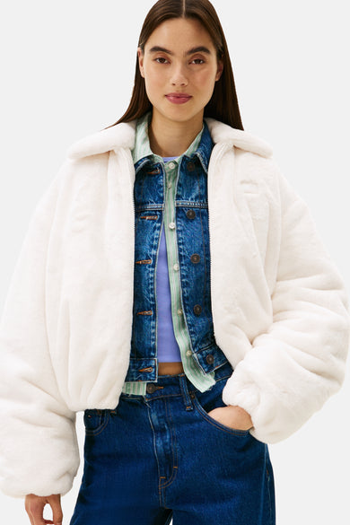 Manteau court blanc de TOMMY JEANS, avec des cheveux longs et sombres et un jeans bleu.