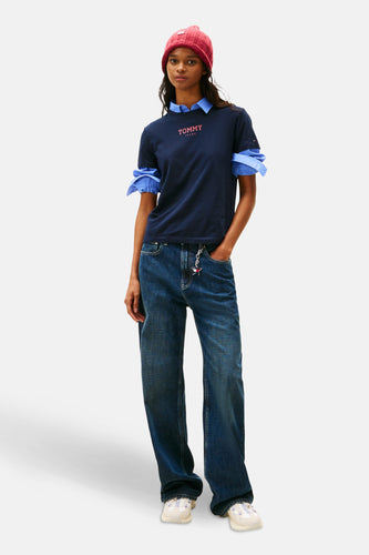 Vrouw in Tommy Jeans outfit met blauw shirt, wijde jeans en roze muts.