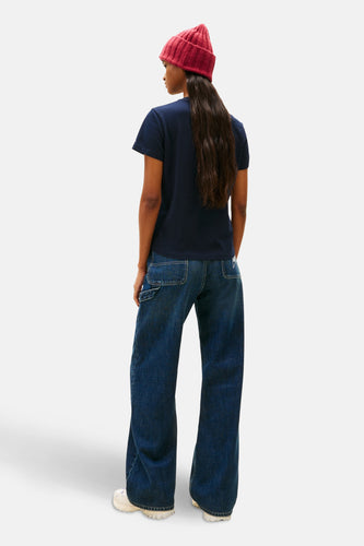 Persoon van achteren in blauw shirt, wijde jeans en rode muts.