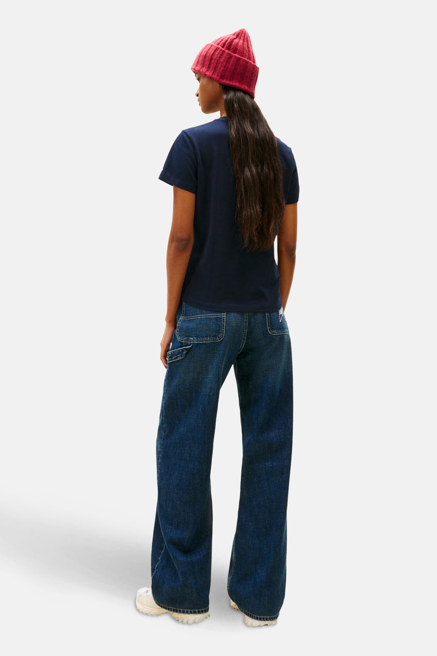 Persoon van achteren in blauw shirt, wijde jeans en rode muts.