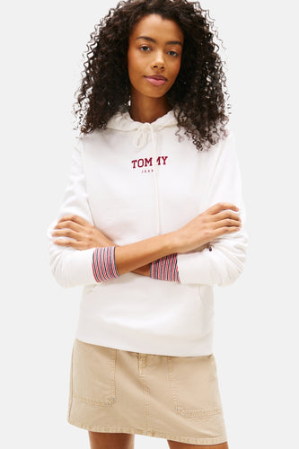 Vrouw in witte hoodie met beige rok, armen gekruist.