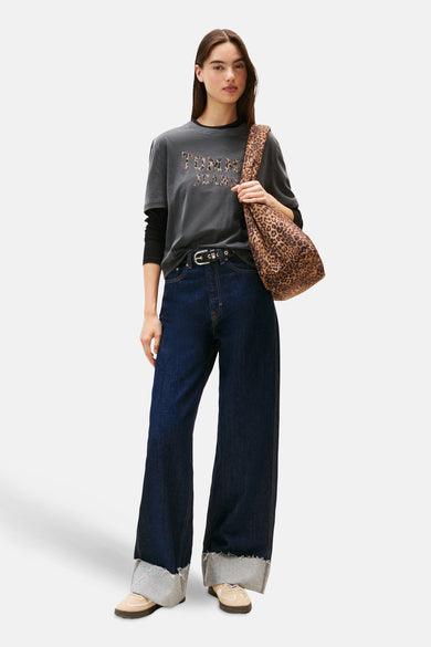 T-shirt gris à manches courtes de TOMMY JEANS, avec des lettres imprimées de panthères, porté avec des jeans foncés, une ceinture et un sac imprimé de panthères.