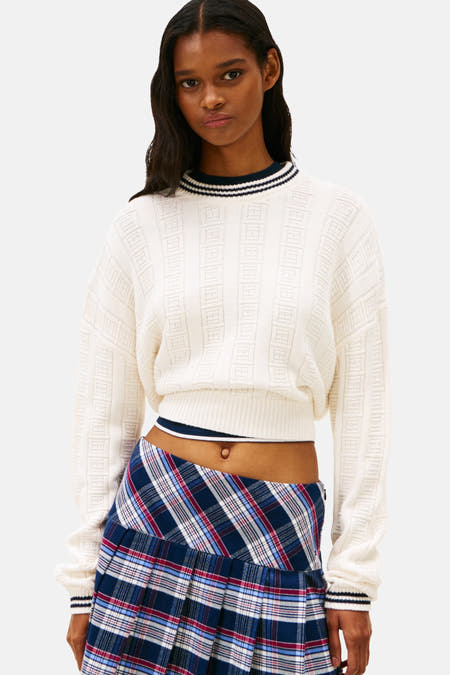 Pull-over blanc avec col rond de TOMMY JEANS, à motif côtelé et une minirobe rayée, chaussettes noires et loafers noirs.