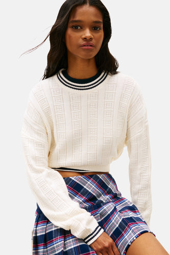 Vrouw draagt witte trui en geruite rok.