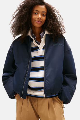 Manteau court bleu de TOMMY JEANS, avec 'TOMMY JEANS' sur le dos et pantalon beige.