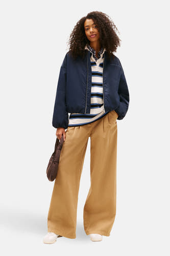 Manteau court bleu de TOMMY JEANS, avec un chemisier rayé, une pantalon brun large et une sacoche.
