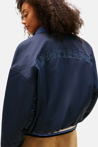 Manteau court bleu de TOMMY JEANS, avec le nom de la marque brodé sur le dos.