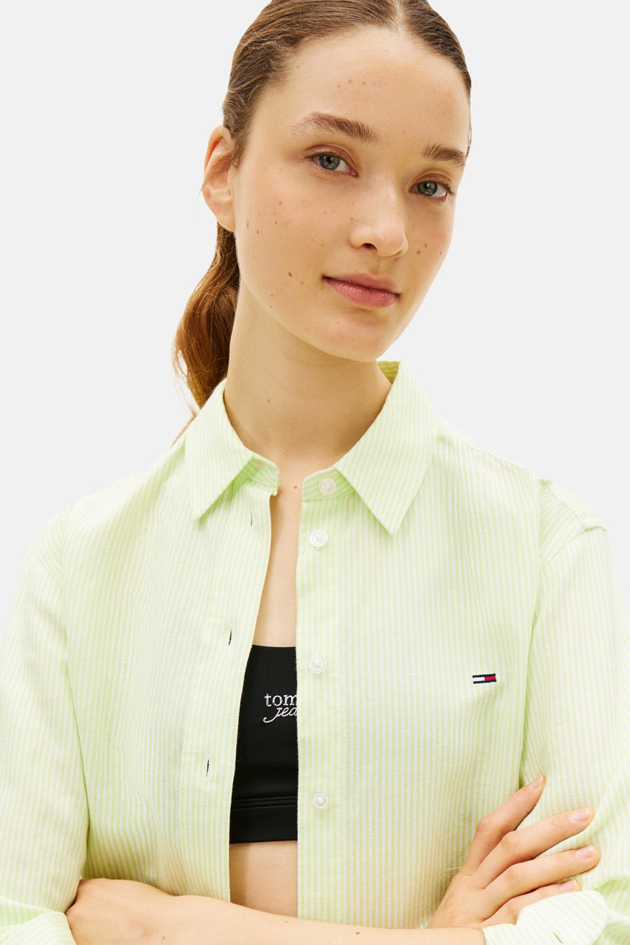 Chemise rayée vert et blanc à manches longues de TOMMY JEANS, oversize, avec logo discret et portée sur un débardeur de sport noir.