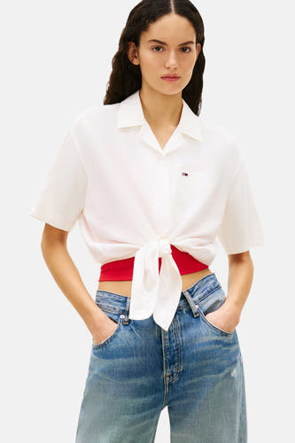 Chemise blanche à manches courtes de TOMMY JEANS, nouée avec un haut rouge et un jean bleu.