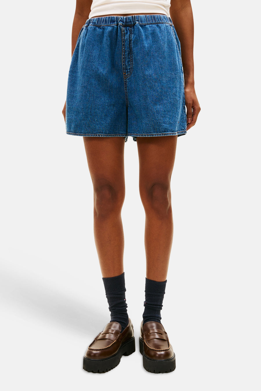 Short en jean bleu moyen de TOMMY JEANS, avec taille élastique, porté avec un t-shirt blanc et une casquette rouge.