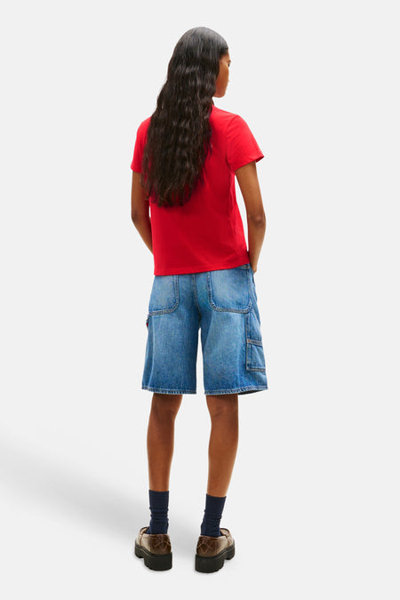 T-shirt rouge TOMMY JEANS, coupe décontractée à manches courtes, associé à un short en jean et des chaussures marron.