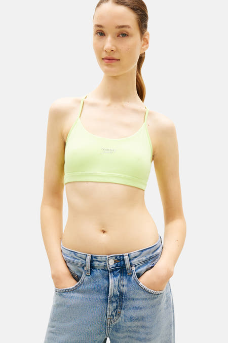 Haut court vert TOMMY JEANS avec logo, porté avec un sweat à capuche gris ouvert et un jean déchiré.