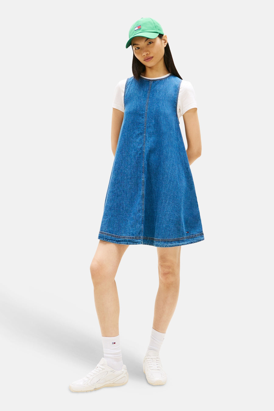 Robe en jean bleu moyen sans manches de Tommy Jeans, combinée avec un t-shirt blanc et une casquette verte.