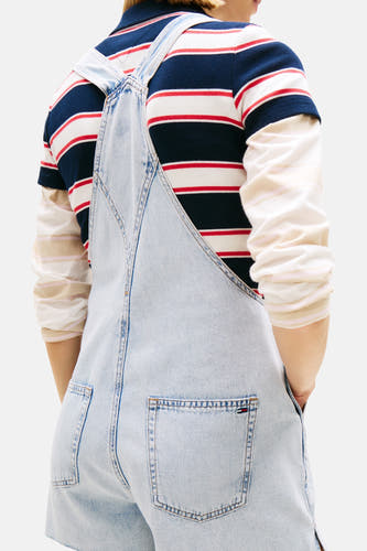 Lichtblauwe denim jumpsuit van TOMMY JEANS, rugzijde met bretels over een gestreept T-shirt.