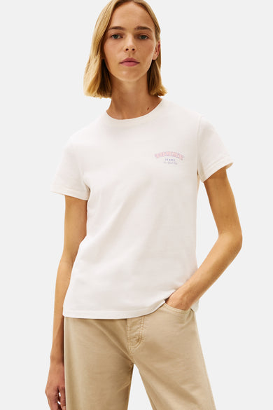 T-shirt écru à manches courtes de TOMMY JEANS, avec une impression colorée sur le dos, associé à un pantalon beige et des baskets blanches.
