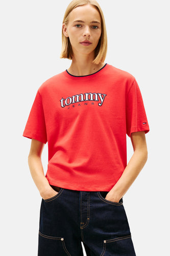 Model met blonde bob in een rode Tommy Jeans T-shirt en donkerblauwe broek, handen in de zakken, op een witte achtergrond.