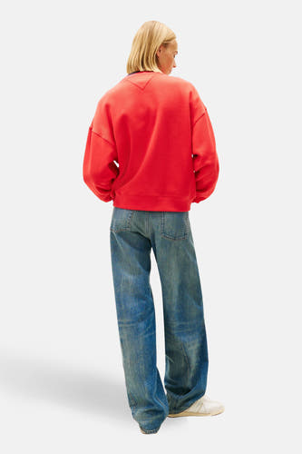 Rode sweater van TOMMY JEANS, gedragen met wijde jeans en witte sneakers, achterkantweergave.
