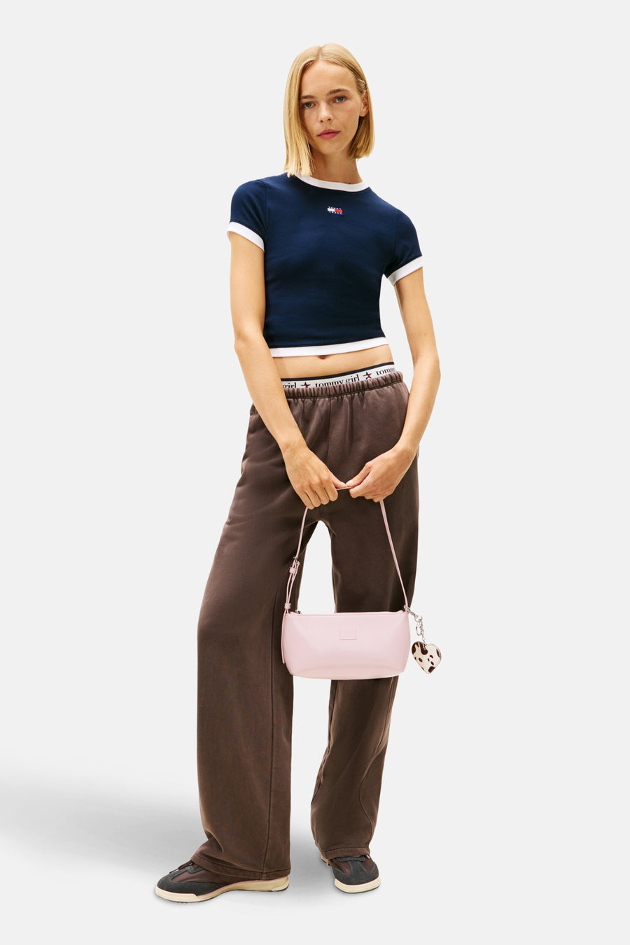 Blauw T-shirt met korte mouwen van TOMMY JEANS, afgewerkt met witte accenten, gedragen met bruine joggingbroek en een roze handtas.