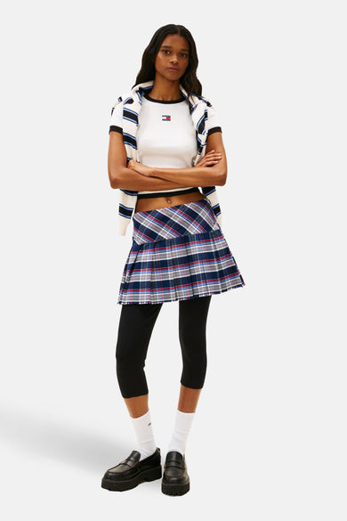 T-shirt blanc à manches courtes de TOMMY JEANS, avec une texture côtelée et un logo, combiné avec une mini-jupe à carreaux et un legging noir.