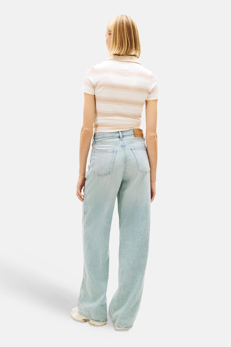 Jeans larges en denim bleu clair de TOMMY JEANS, avec jambes larges et poches arrière, combinées avec un polo rayé.