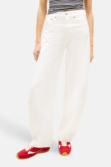 Jean large blanc cassé de TOMMY JEANS, porté avec un crop top rayé et des baskets rouges.