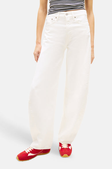 Jean large blanc cassé de TOMMY JEANS, porté avec un crop top rayé et des baskets rouges.