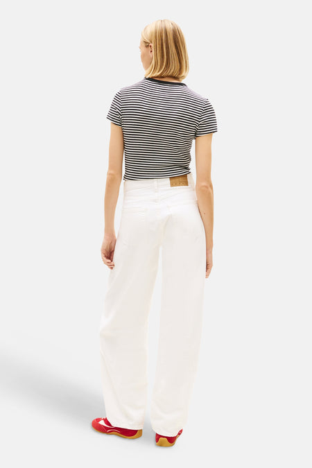 Jean en denim blanc cassé à jambes larges de TOMMY JEANS, vus de dos, avec une étiquette en cuir à la taille, portés avec une chemise rayée et des baskets rouges.