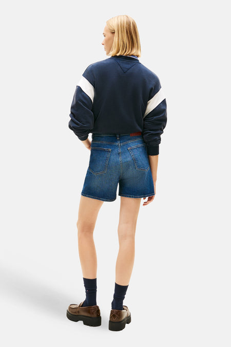 Short en jean bleu marine de Tommy Jeans, avec poches et une ceinture rouge, combiné avec un sweat-shirt bleu marine.