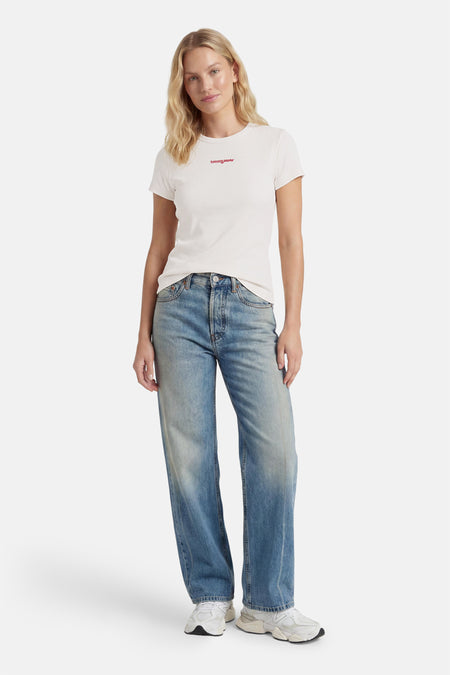 Witte korte mouwen T-shirt van TOMMY JEANS met rode logo op borst, gedragen met blauwe jeans en witte sneakers, front view