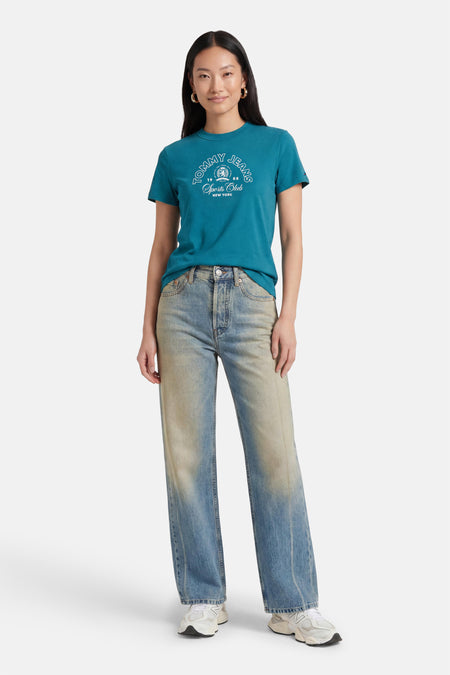 Groene korte mouwen t-shirt van TOMMY JEANS met wit logo, gedragen met gecombineerde jeans en witte sneakers, front view