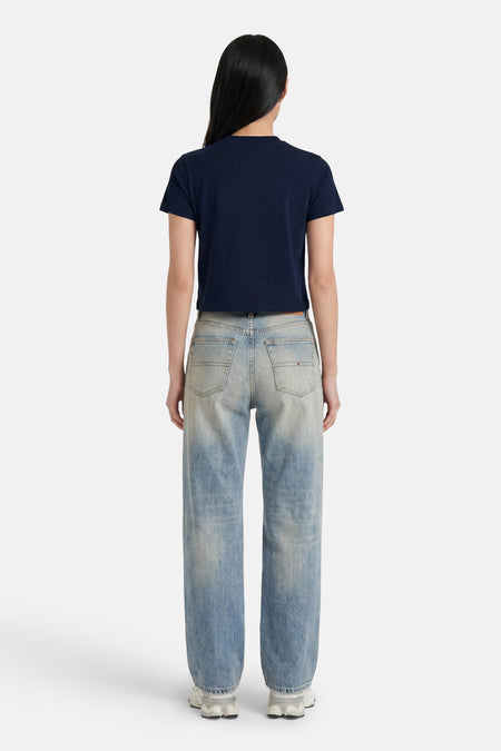 Donkerblauwe korte mouwen T-shirt van TOMMY JEANS, achterzijde, met ronde hals en strakke pasvorm, gedragen met lichtblauwe jeans en witte sneakers.