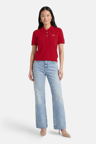 Rode korte mouwen polo van TOMMY JEANS met gebreide textuur en wit logo, gedragen met lichtblauwe jeans en goudkleurige hoge hakken, front view.
