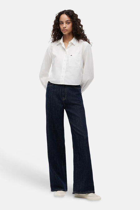 Donkere blauwe wijde jeans van TOMMY JEANS, met rechte pijpen en klassieke denimtextuur, gedragen met wit overhemd en sneakers, front view.