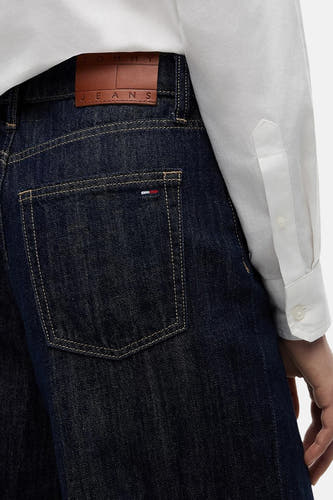 Donkere blauwe wide-leg jeans van TOMMY JEANS, met bruin leerlabel en contrastnaden, close-up van achterzak, model draagt wit overhemd