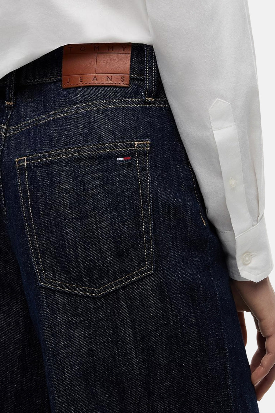 Donkere blauwe wide-leg jeans van TOMMY JEANS, met bruin leerlabel en contrastnaden, close-up van achterzak, model draagt wit overhemd