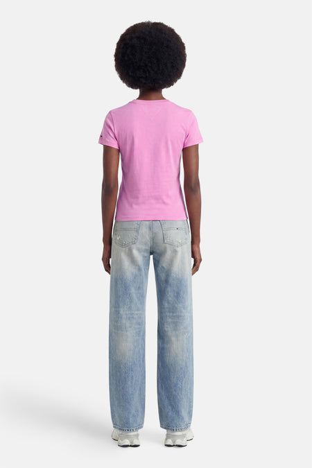 Roze korte mouwen T-shirt van TOMMY JEANS, achterzijde weergegeven, met klein logo op mouw, gedragen met lichtblauwe jeans en witte sneakers.