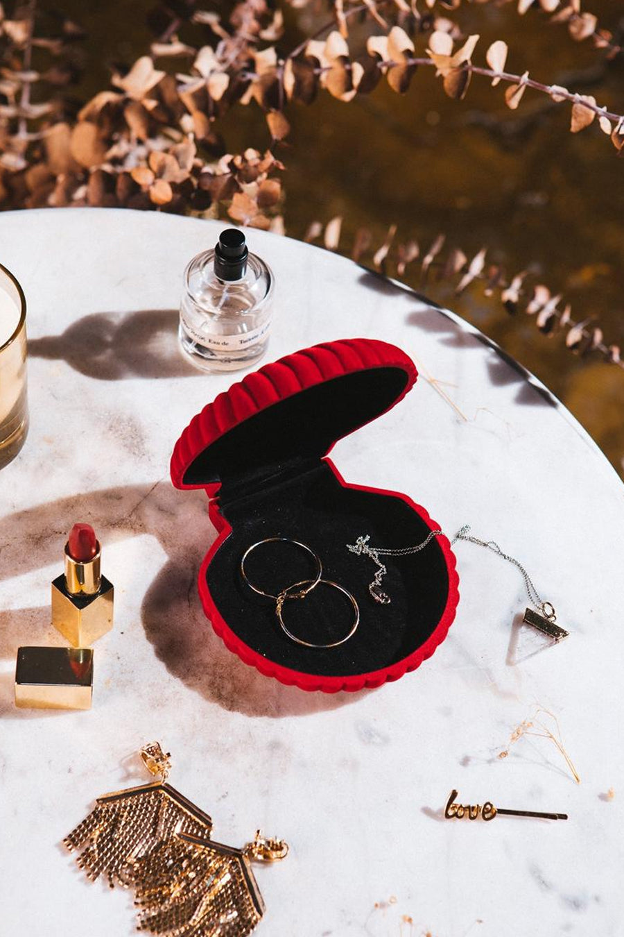 Rode fluwelen hartvormige sieradenkist van THE WOW EFFECT COMPANY, open met gouden ringen en ketting, op marmer met accessoires en droge bloemen.