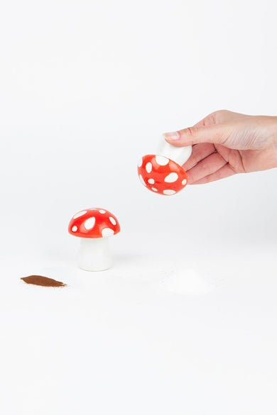 Champignon rouge piment et sel de DOIY, avec des taches blanches, avec une main qui secoue sur un fond blanc.
