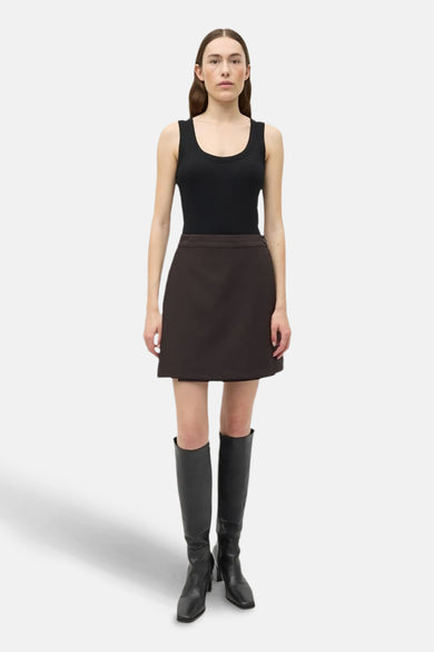 Jupe courte brune d'ENVII portée avec un tank-top noir et des bottes noires jusqu'aux genoux.