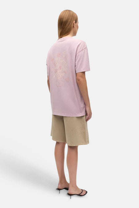 T-shirt rose d'ENVII avec imprimé floral ton sur ton au dos, combiné avec un short kaki et des sandales noires.