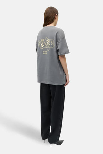 T-shirt gris à manches courtes ENVII, avec imprimé graphique au dos, combiné avec un pantalon noir et des escarpins.