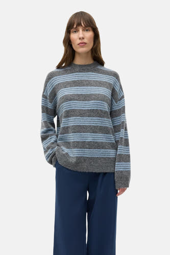 Pull gris à col rond d'ENVII, avec des rayures bleues et porté avec un pantalon bleu foncé.