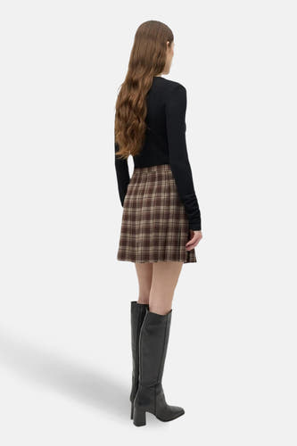 Jupe courte brune d'ENVII avec un motif à carreaux, associée à une chemise noire et des bottes jusqu'aux genoux.