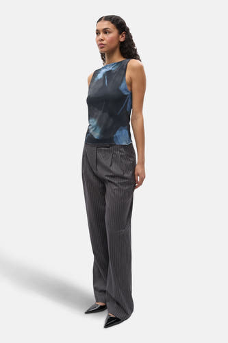 Zwarte mouwloze top van ENVII, met blauwe bloemmotieven, gecombineerd met een grijze gestreepte pantalon en zwarte schoenen.