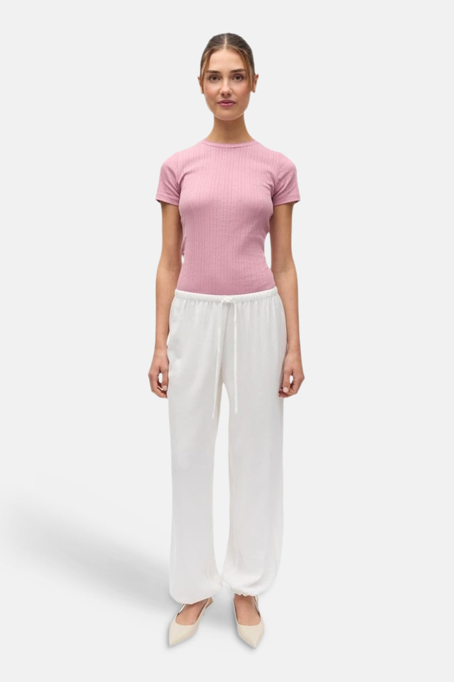 Pantalon blanc d'ENVII avec cordon de serrage et coupe décontractée, porté avec un haut rose et des chaussures claires.