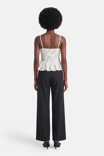 Chemisier blanc sans manches en dentelle d'ENVII avec bretelles spaghetti et ourlet péplum, porté avec un pantalon noir et des mules, vue arrière.
